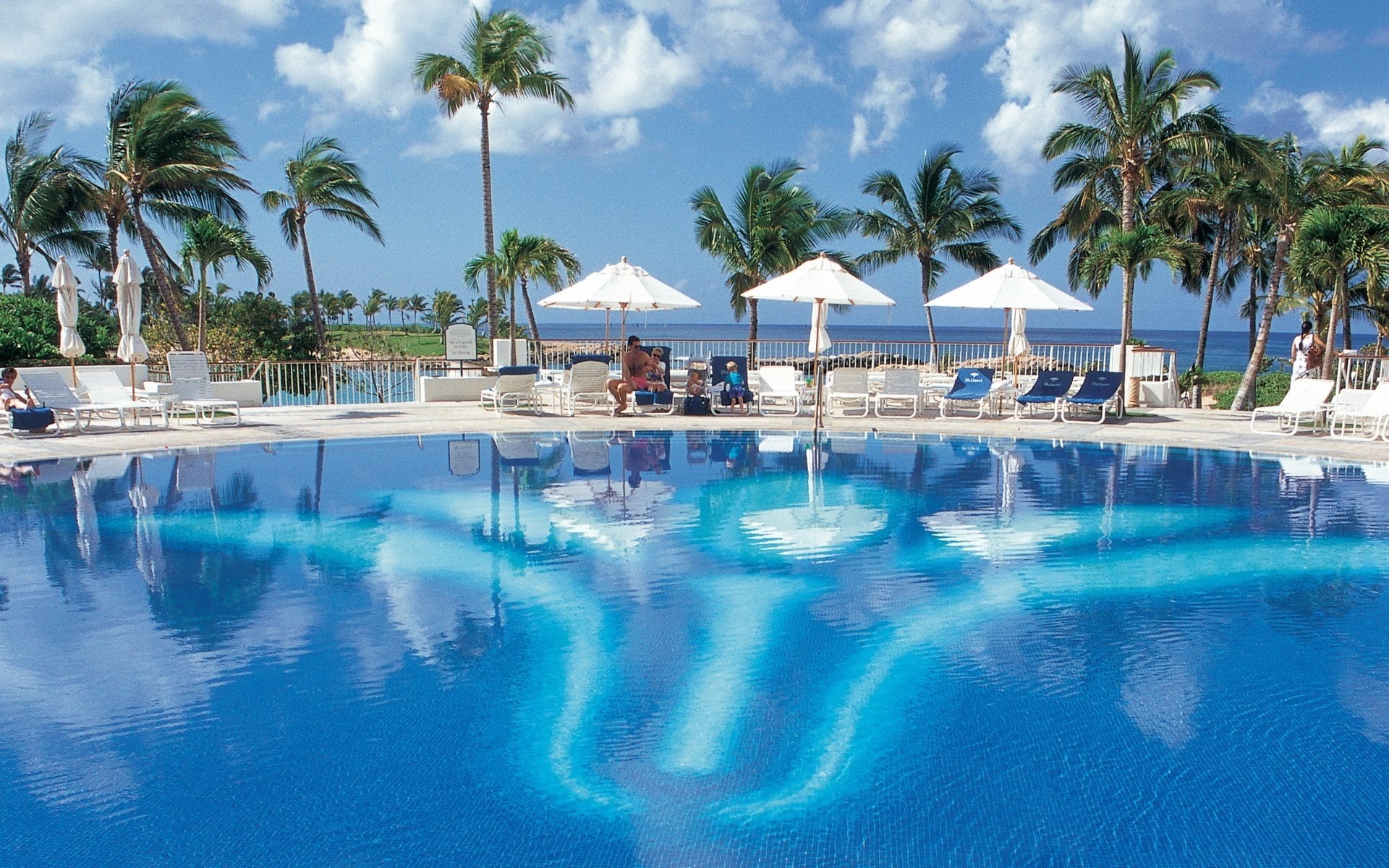 blue water in the pool wind umbrellas beach water sky resort palm trees vacation hotel vacation sun beds pool sea vacationers clouds heat heat summer reflection