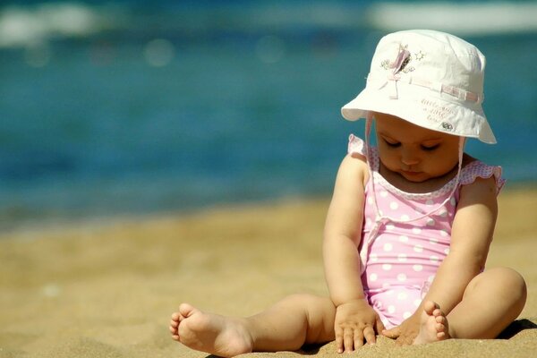 Eine kleine Fashionista mit einem Hut im Sand am Meer. Badeanzug mit Punkte