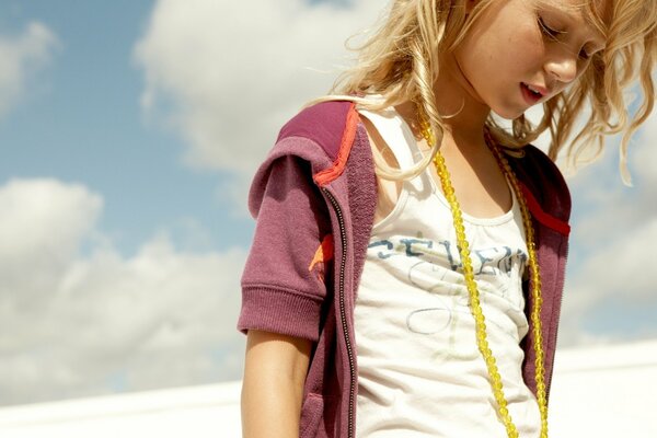 A blonde girl with yellow beads on her neck against a cloudy sky