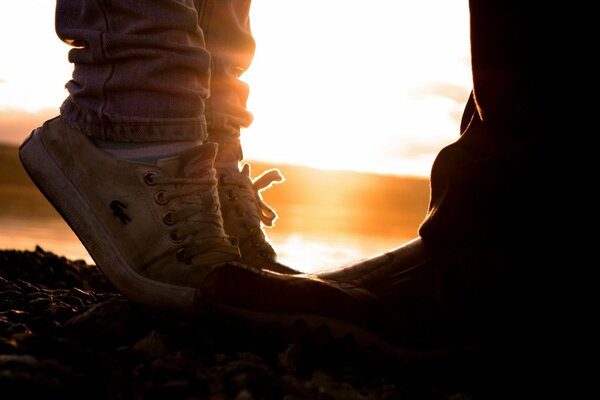 Dos pares de zapatos-ella y él en el fondo de la puesta del sol