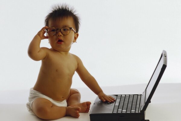 Petit enfant à lunettes assis derrière un ordinateur portable