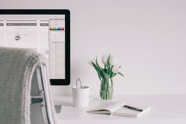 Weißer Tisch mit Buch, Blumenvase und Computer