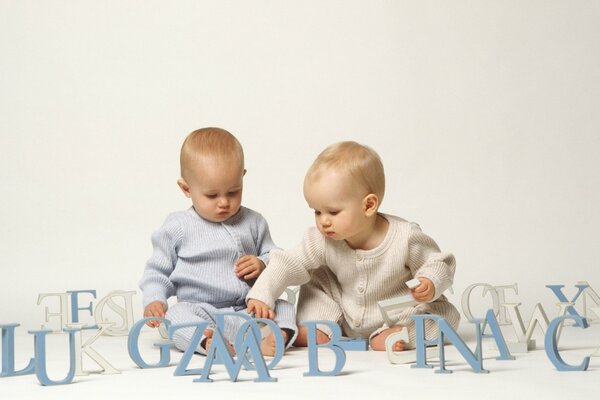 Two little boys sitting in three-dimensional letters. In blue and white tones