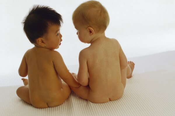 Two naked babies are sitting with their backs