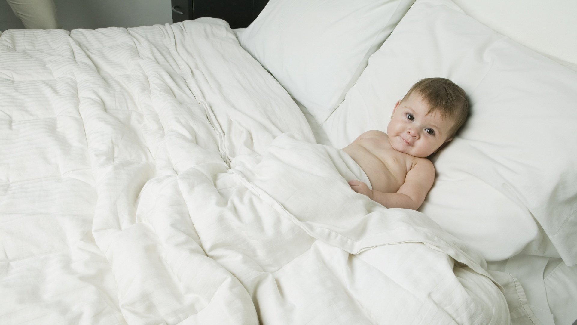 dans le lit des parents se préparer à dormir visage satisfait blanc regard visage yeux bébé enfant miette fidget egoza lit draps blancs lit yeux