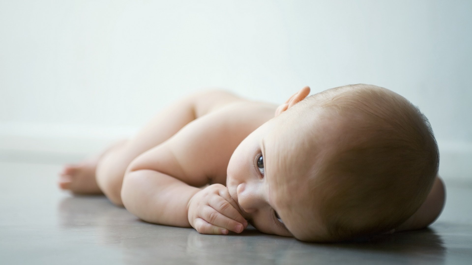 pequeño aburrido acostado en el suelo desnudo mirada bebé bebé miga miente