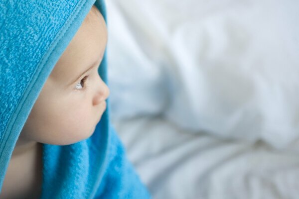 The child is sitting in a blue towel after bathing