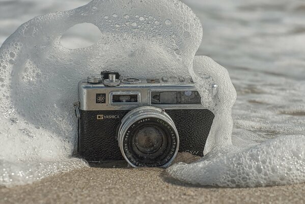 A camera on the sand that is washed away by a wave