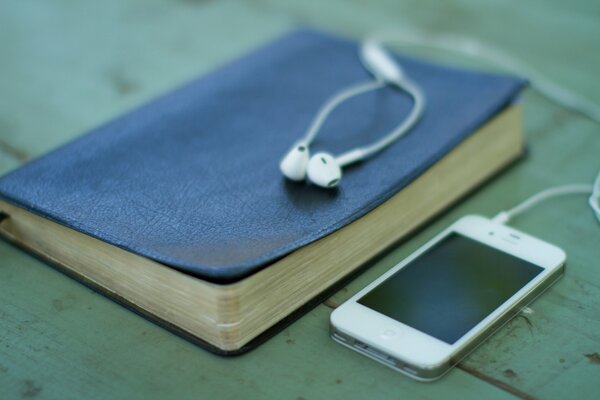 An iPhone with headphones and a blue book next to it