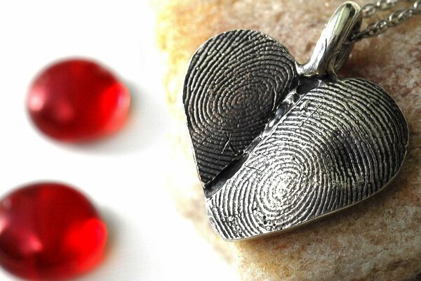 Heart-shaped pendant made of fingerprints on a background of red pebbles