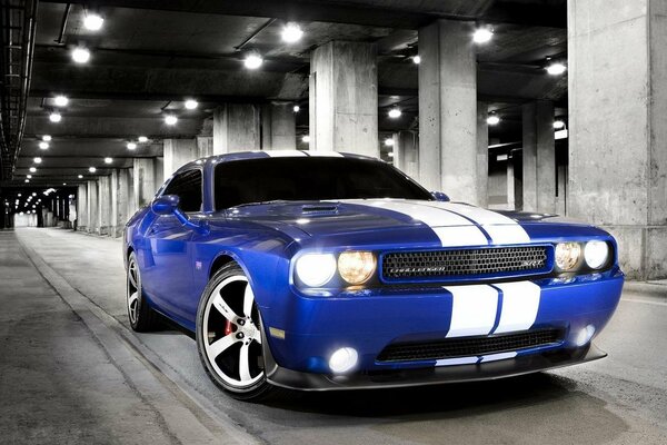 A blue sports car with white stripes and headlights on