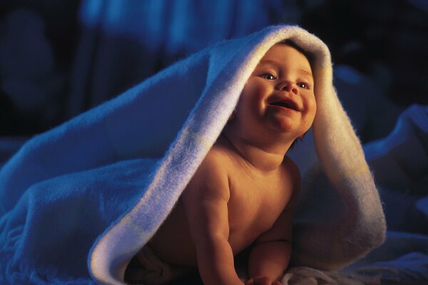 A baby smiles under a white blanket