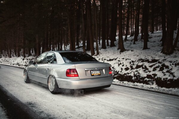 Authentic Audi white car among the snow-covered forest and road