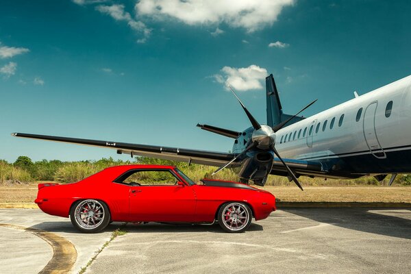 Chevrolet rojo brillante cerca del avión