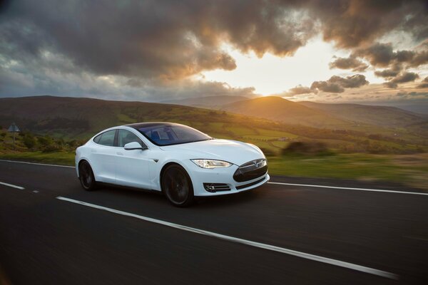 Weißes Tesla Model s auf dem Hintergrund von Straßen, Hügeln und Wolken