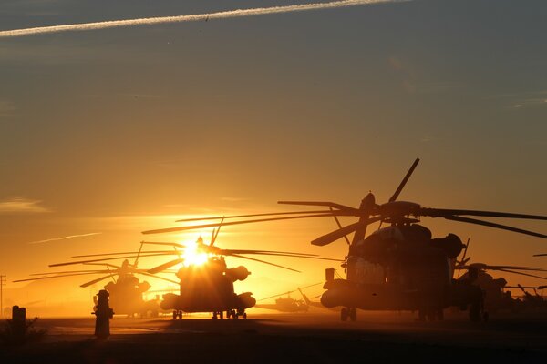 Kilka helikopterów stoi o zachodzie słońca