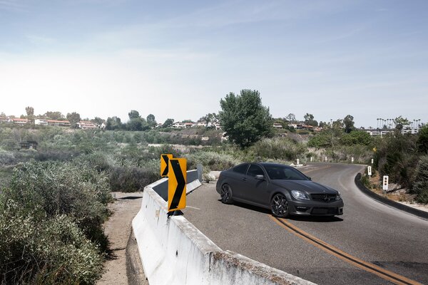 A black matte car stands half-side on a fenced road