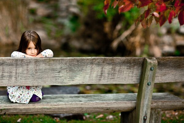 A girl on a bench by an autumn tree