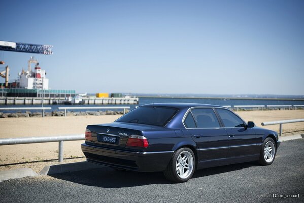 BMW e38 740il black parked near the beach side view against the background of the sea and port structures