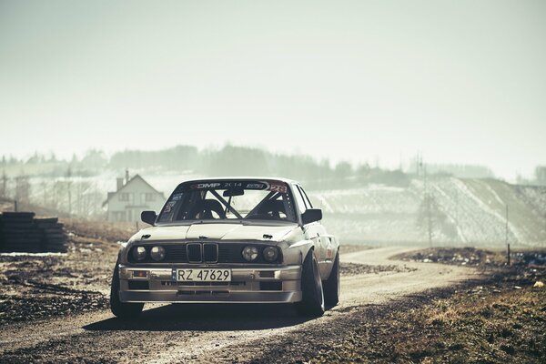 BMW E30 de plata en el sol en la carretera