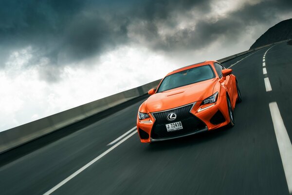 Orange Lexus rushes along the highway under a nightmarish sky