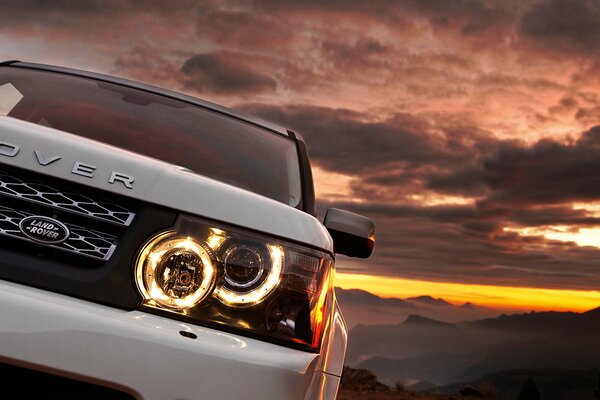 Weißes Auto bei Sonnenuntergang Berge. Range Rover mit neuen Scheinwerfern