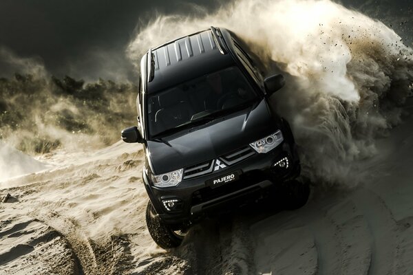 Чёрный Mitsubishi Pajero на песке в клубах пыли