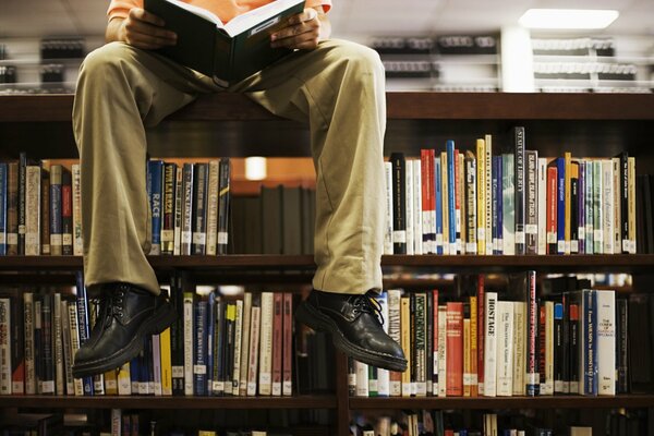 Un uomo legge un libro su una libreria in biblioteca