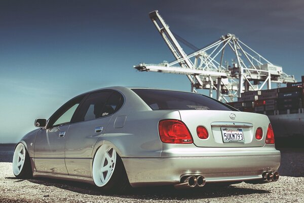 Silver Lexus with extinguished headlights. In the background is a port crane