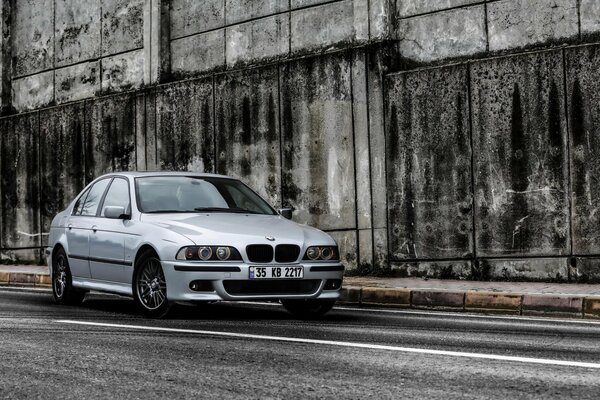 A silver bmw 528i is standing near the wall