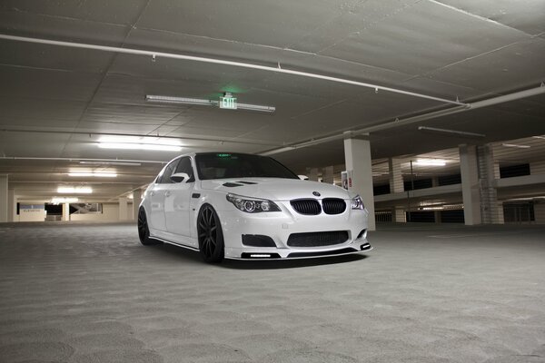 A white BMW is driving through an underground parking lot