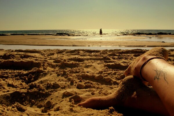 Legs with a tattoo on the beach under a romantic sunset