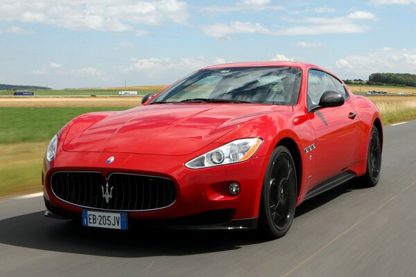 A scarlet car rushes across the field on a summer day