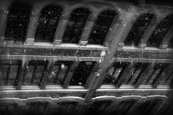 Foto en blanco y negro de un edificio antiguo con ventanas en invierno con nieve cayendo