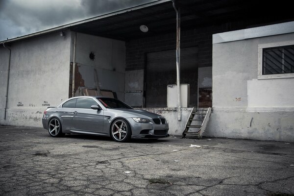 A gray BMW is standing on the asphalt near the warehouse