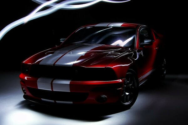 Automóvil Ford color rojo con dos rayas blancas en un ambiente oscuro