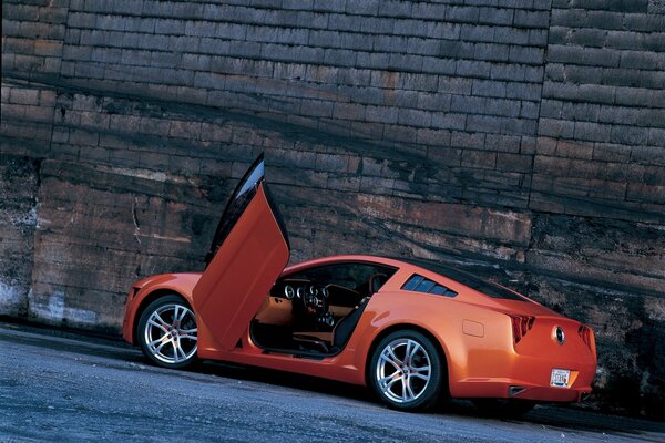 On the background of a stone wall - a red Ford Mustang with an open door