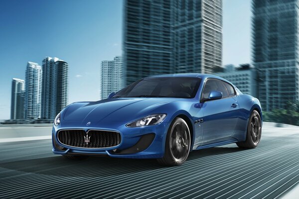 A blue Maserati car rushes across the bridge of a modern city