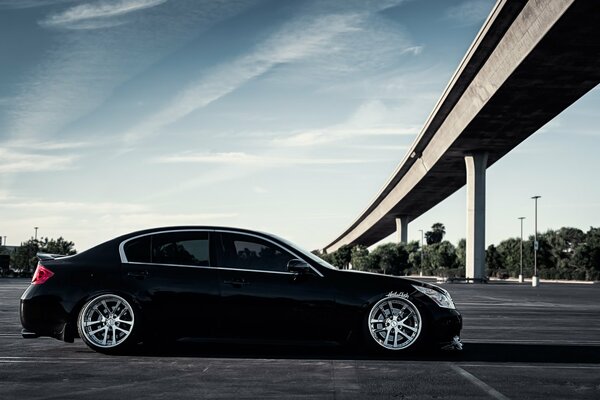 The black Infiniti g37 car is under the bridge