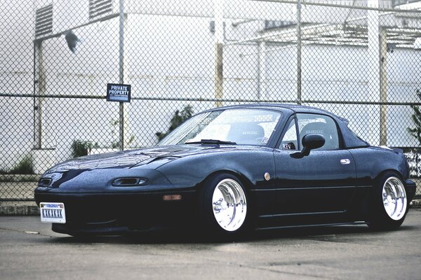 Black mazda miata on the background of a fence with a grid