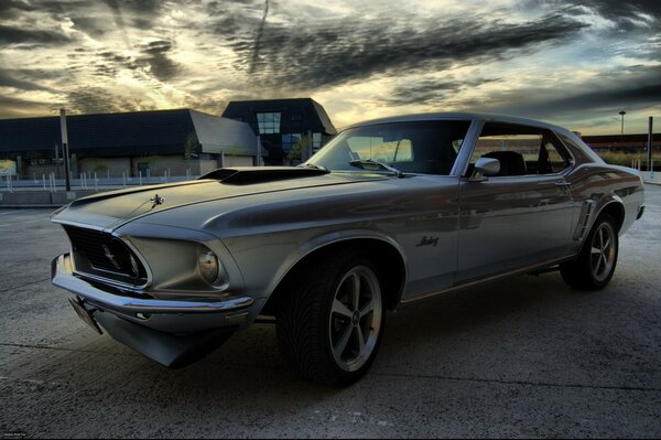 Un Mustang plateado contra el cielo nublado y las casas