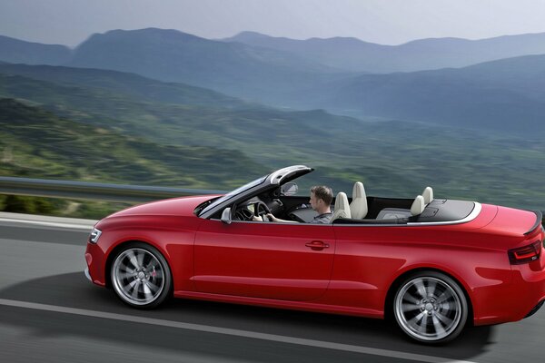 A guy rides a convertible in a mountain landscape