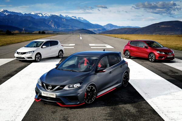 Le auto Nissan di diversi colori stanno sulla strada sullo sfondo delle montagne innevate