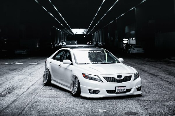 A white Toyota camry stands in the middle of the road