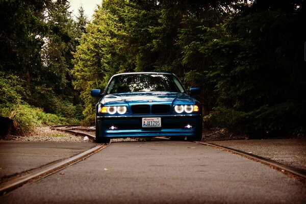 Un bmw E38 azul tintado con faros geniales monta en una carretera suburbana