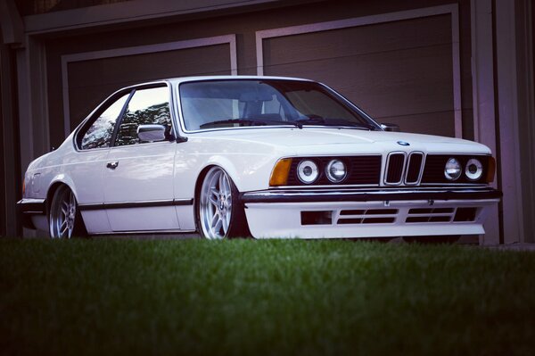 White classic bmw e24 on the background of green grass and garage