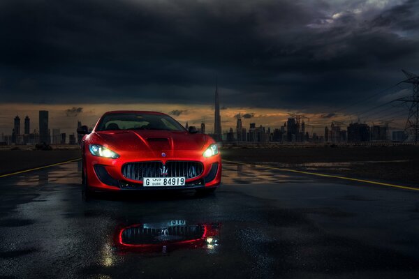 Red sports Maserati with headlights on at night against the background of the city