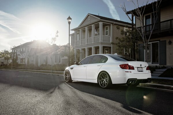 A white BMW m5f10 is parked on the road under a sunny sky