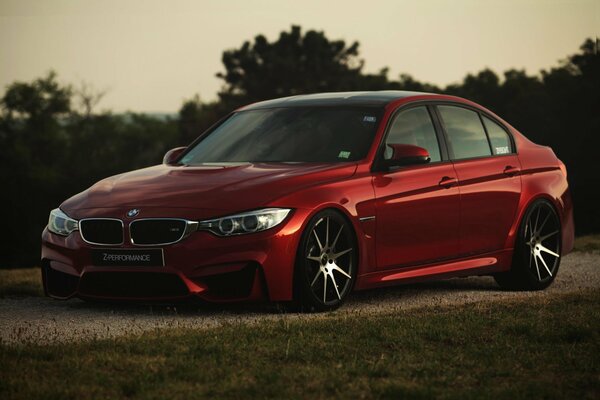 Red bmw f80 m3 on the background of a dirt road and trees