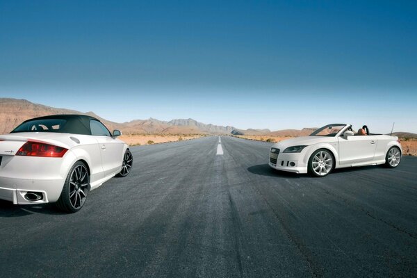 Two white convertibles are standing on the road